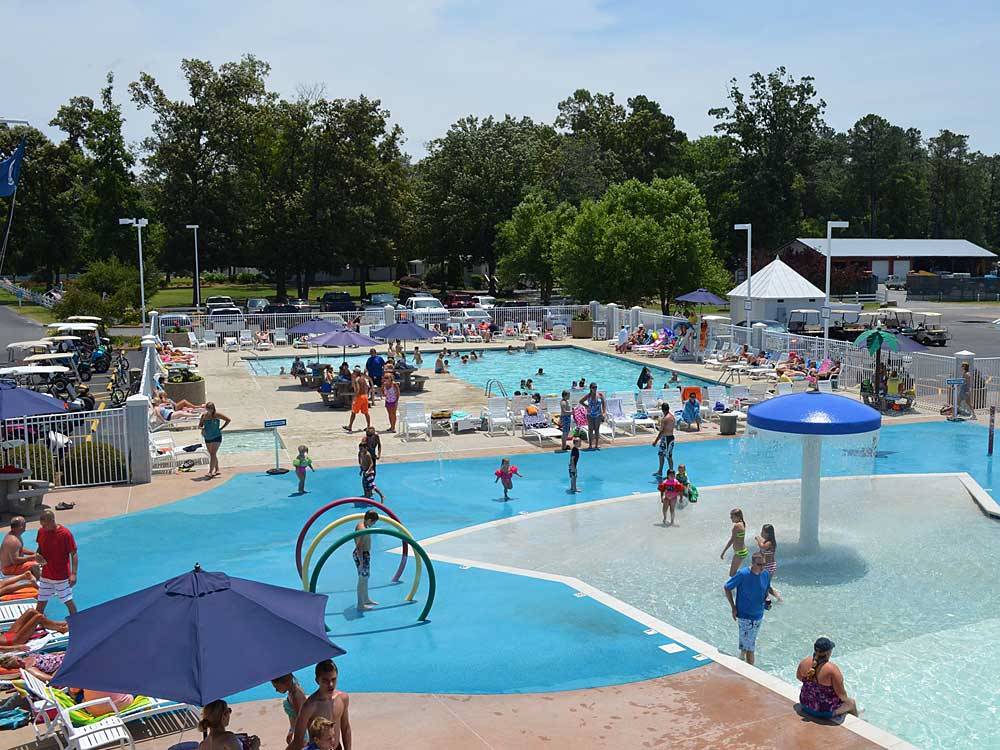Campground guests gather around pool and splashpad for kids.