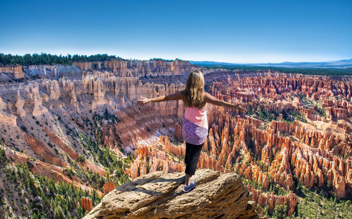 Woman standing on lookout point over a canyon filled with hoodoos.