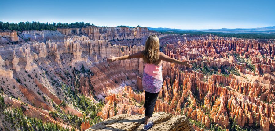 Woman standing on lookout point over a canyon filled with hoodoos.