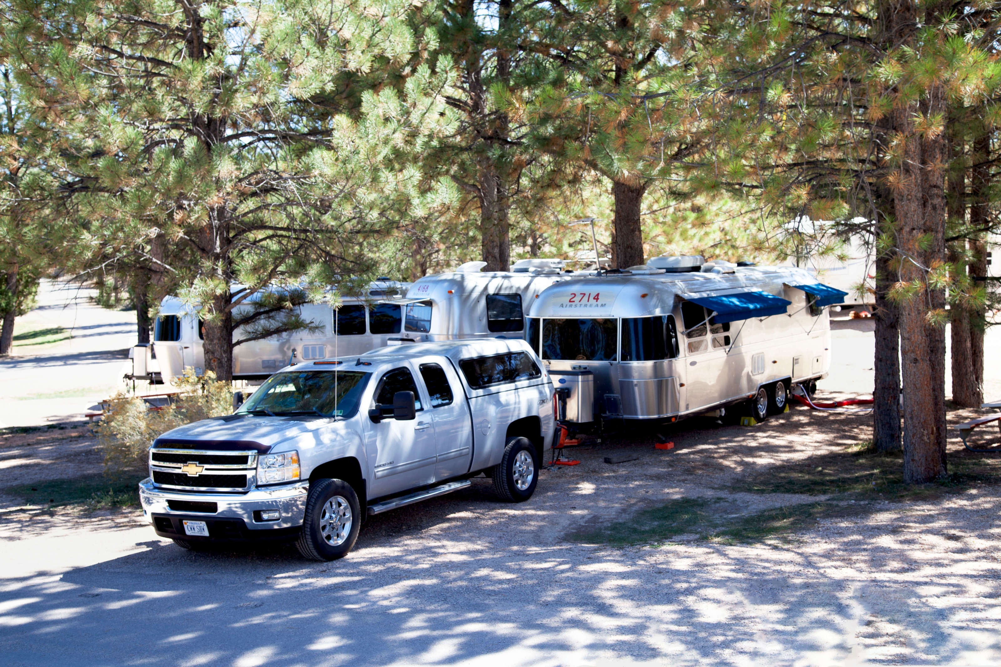 Truck hitched to airstream in shady campsite.