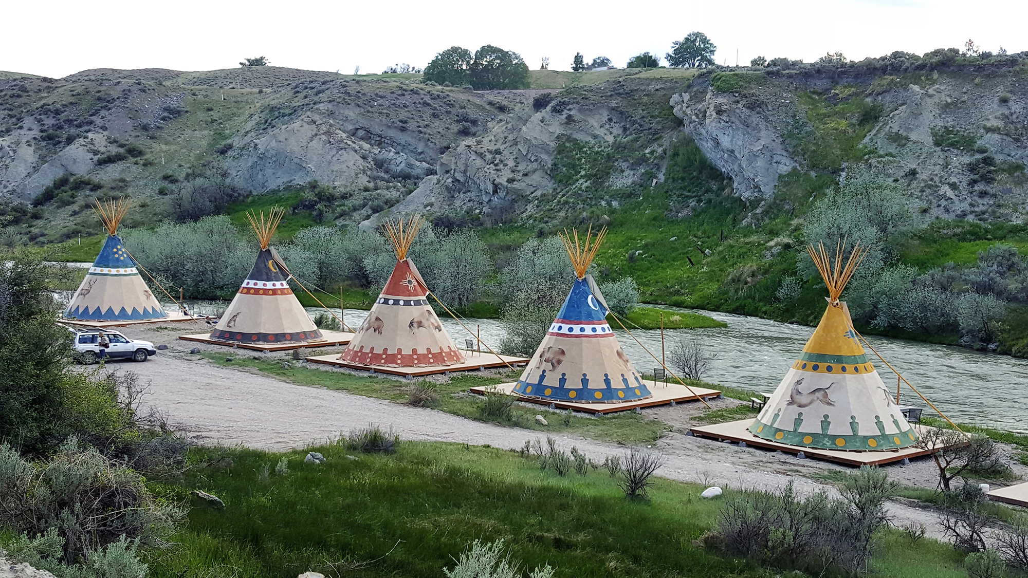Four colorful tipis on the banks of a robust stream.