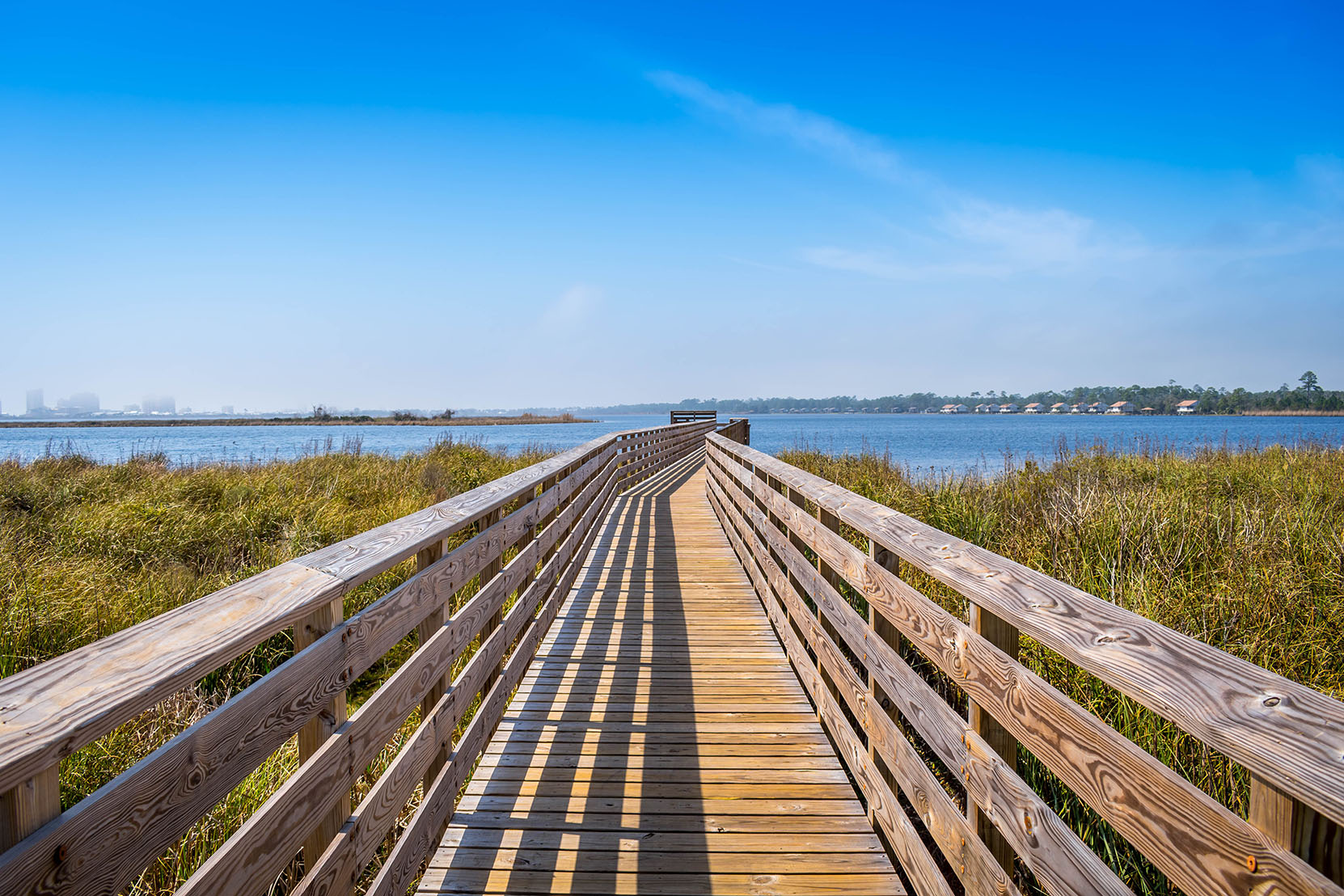 A long boardwalk stretches toward the sea under a blue sky.