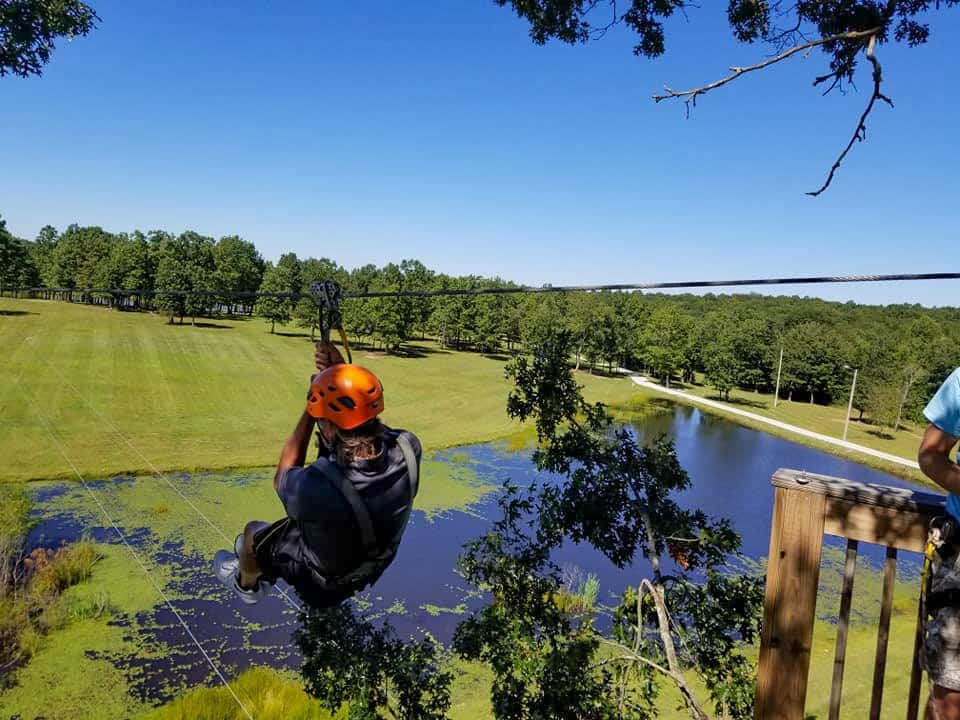 A young person ziplines over a pond.