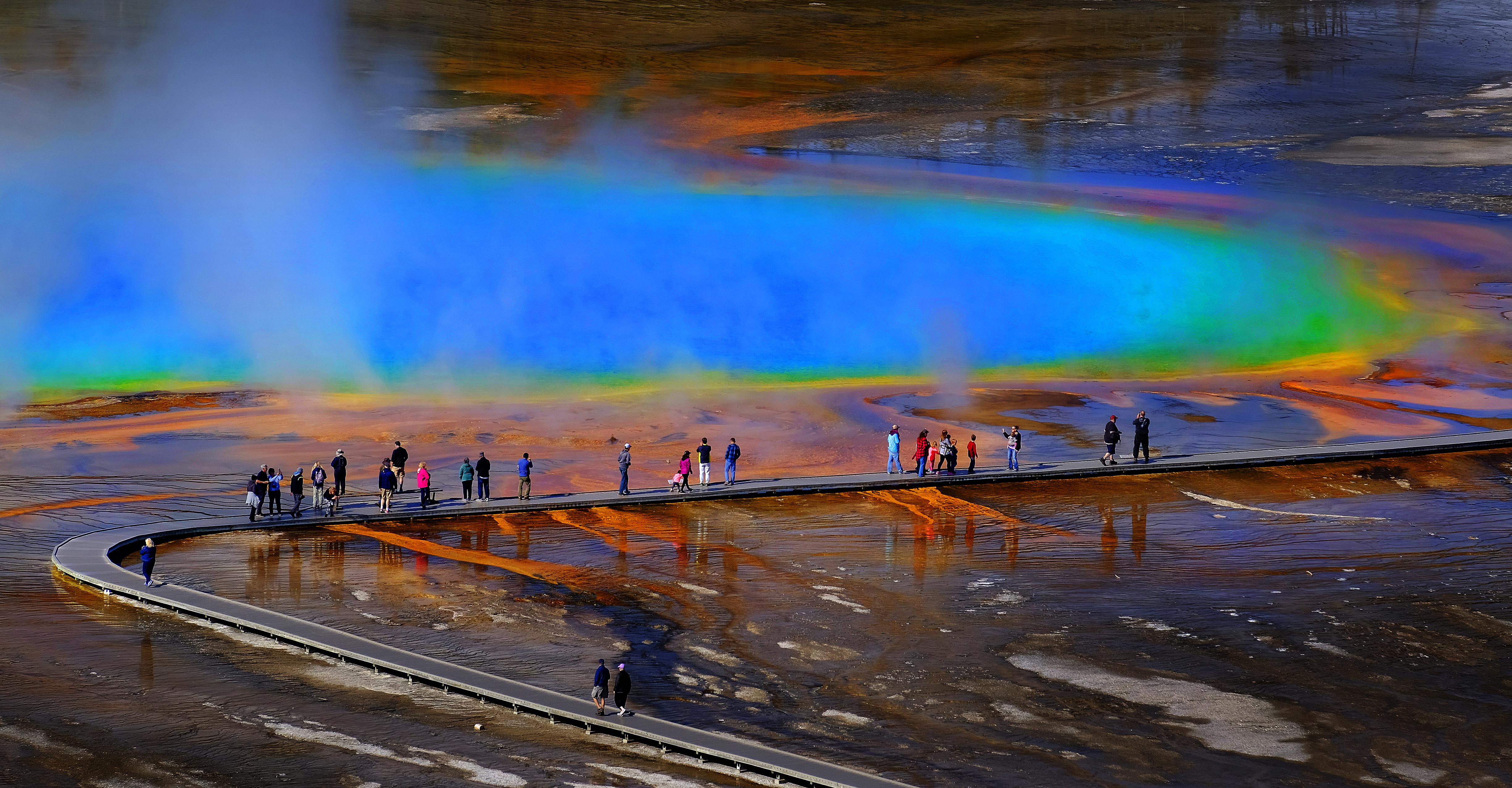Tourists amble on a boardwalk that stretches over a volcanic spring. 