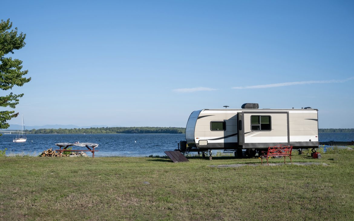 Travel trailer with slideout parked on the grassy banks of a sprawling lake.