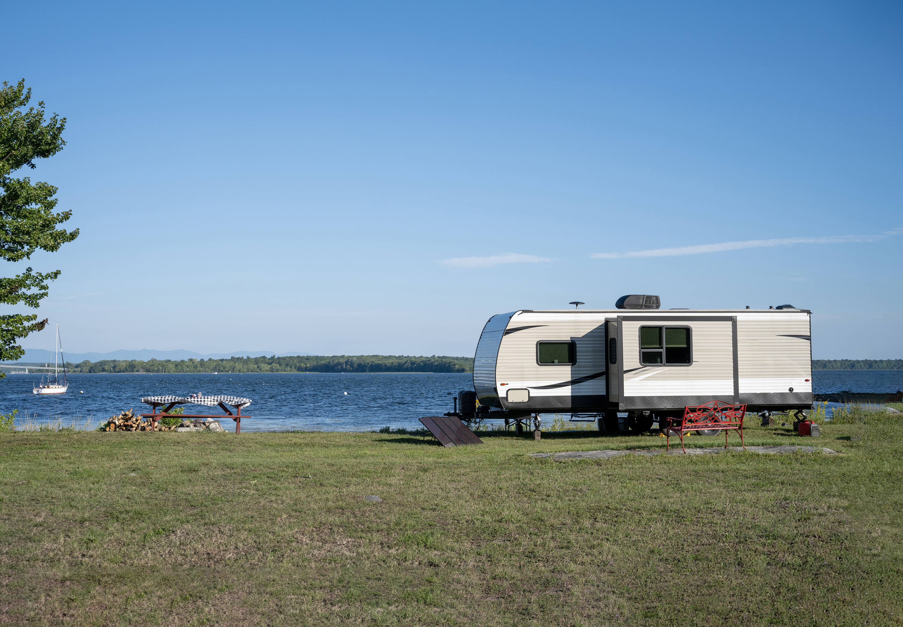 Travel trailer with slideout parked on the grassy banks of a sprawling lake.