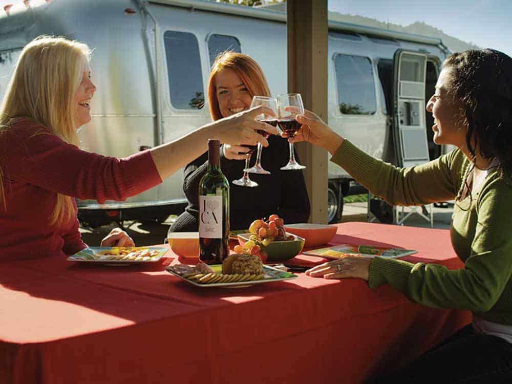 Three women enjoying wine near Airstream motorhome.