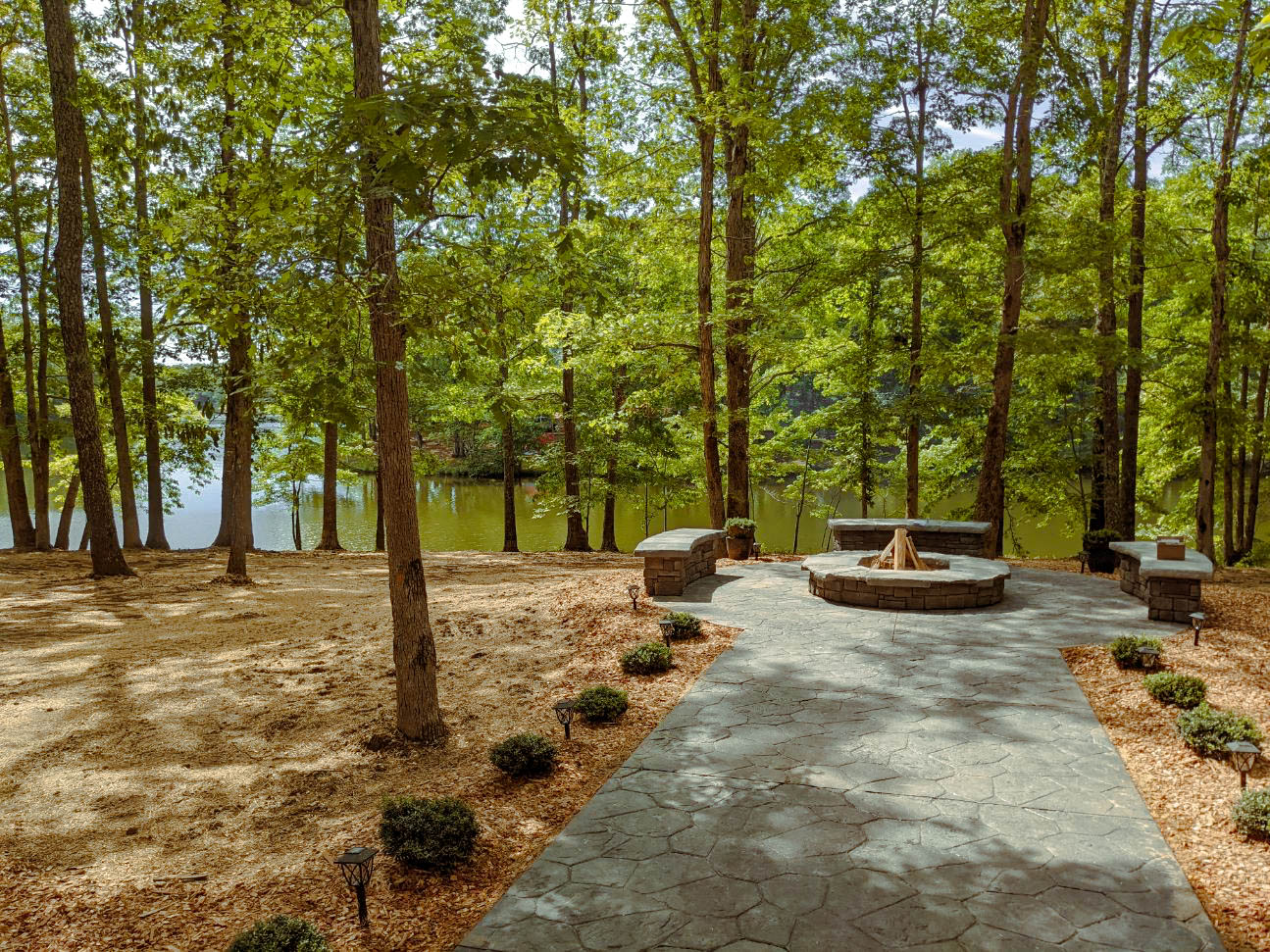 A paved path leading to a fire pit on the banks of a river.